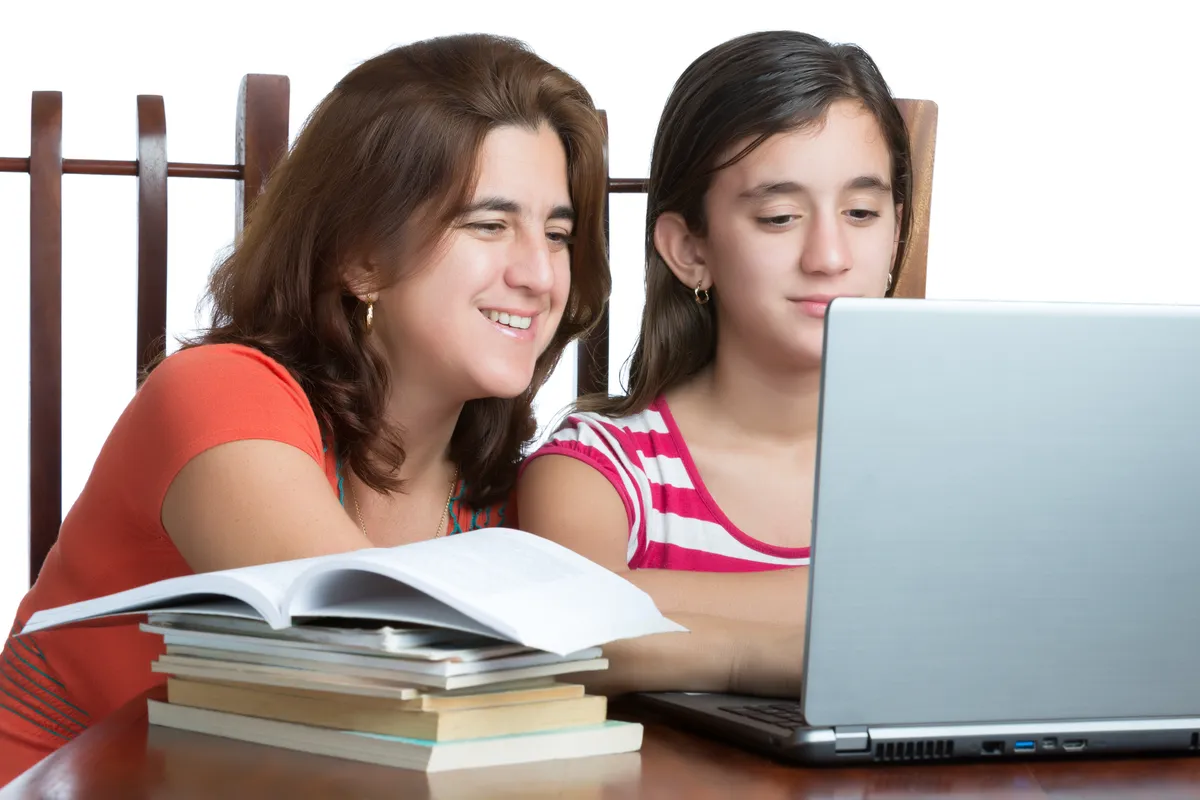A mother and daughter looking at a laptop beside open books.